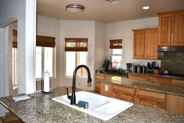 kitchen featuring backsplash, black gas stovetop, sink, and light stone counters