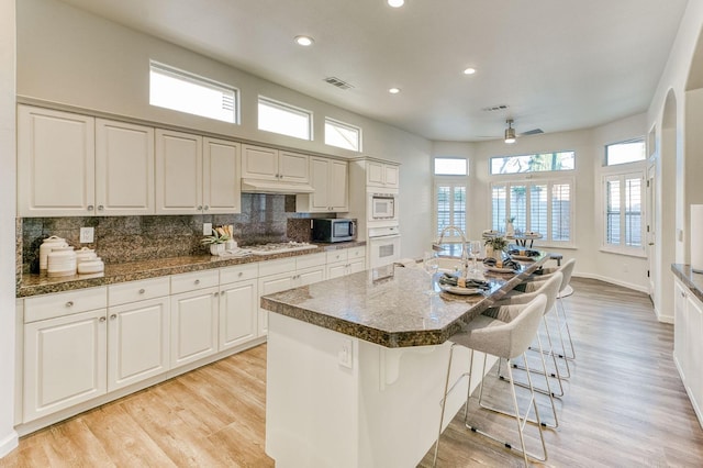 kitchen featuring a breakfast bar, tasteful backsplash, an island with sink, white cabinetry, and white appliances