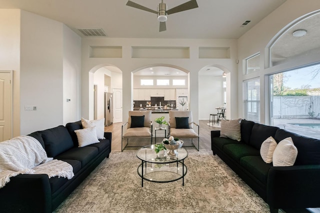 living room with ceiling fan, a towering ceiling, and light wood-type flooring