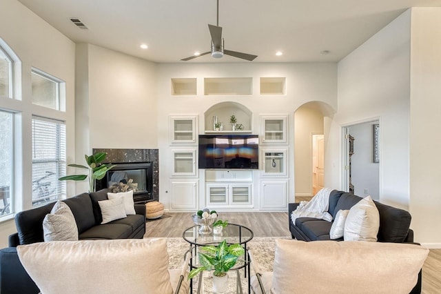 living room featuring a towering ceiling, a high end fireplace, ceiling fan, and light wood-type flooring