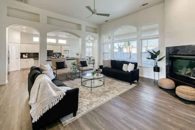 living room featuring ceiling fan, a towering ceiling, and light wood-type flooring