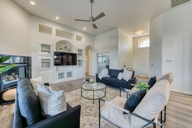 living room with light hardwood / wood-style flooring, built in features, ceiling fan, and a high ceiling