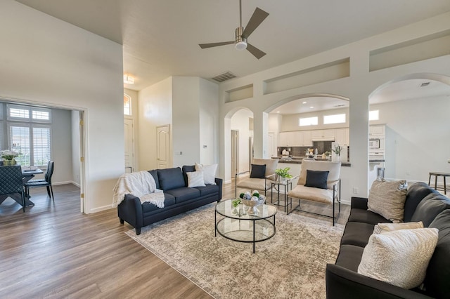 living room featuring light hardwood / wood-style flooring, ceiling fan, and a high ceiling