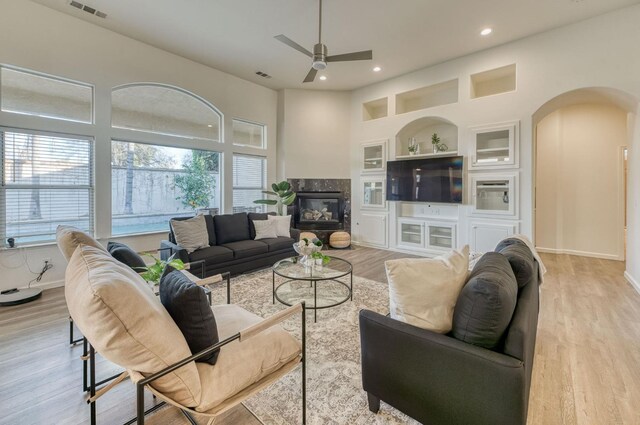 living room featuring built in shelves, ceiling fan, a high end fireplace, and light hardwood / wood-style floors