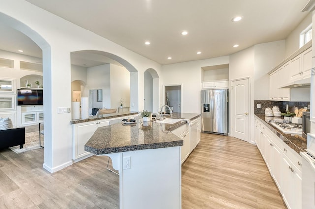 kitchen featuring sink, appliances with stainless steel finishes, light hardwood / wood-style floors, white cabinets, and a center island with sink