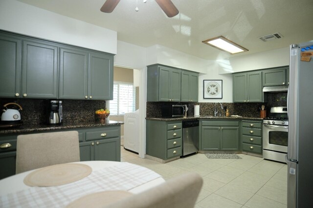 kitchen with sink, green cabinetry, dark stone countertops, light tile patterned floors, and appliances with stainless steel finishes