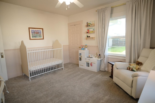 carpeted bedroom with ceiling fan and a crib