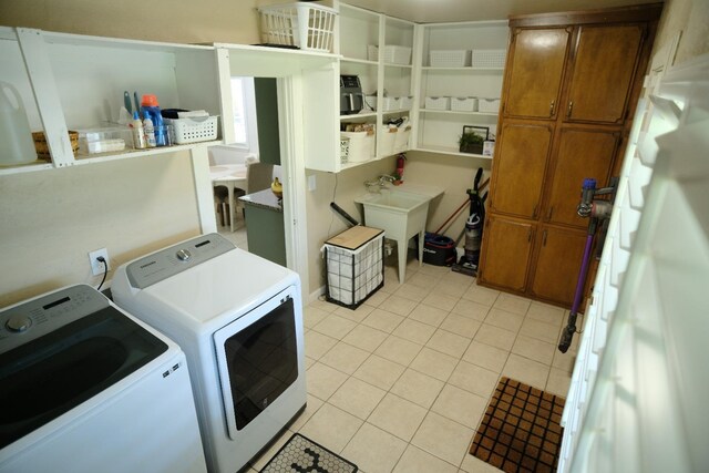 clothes washing area with washer and clothes dryer, light tile patterned floors, cabinets, and sink