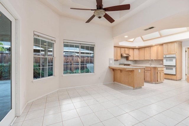 kitchen featuring white double oven, light brown cabinets, a raised ceiling, tasteful backsplash, and light tile patterned flooring