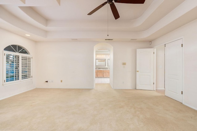 carpeted empty room with a raised ceiling and ceiling fan