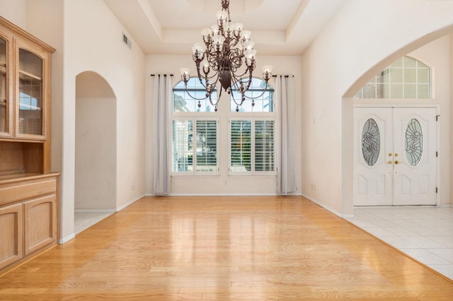 unfurnished dining area with a tray ceiling, french doors, light hardwood / wood-style floors, and a notable chandelier