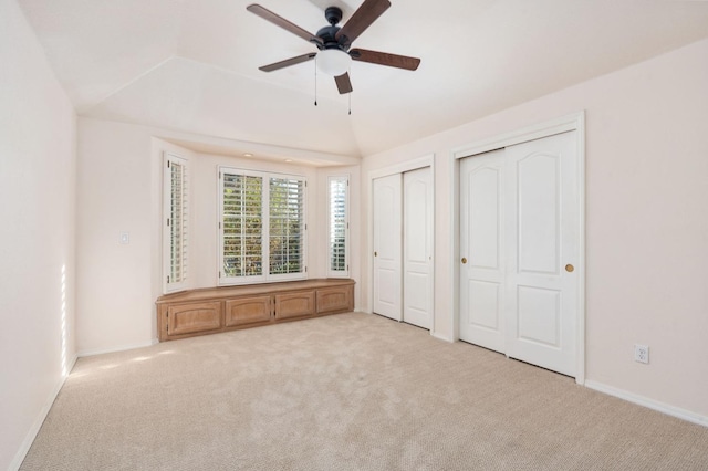 unfurnished bedroom with vaulted ceiling, ceiling fan, light colored carpet, and two closets