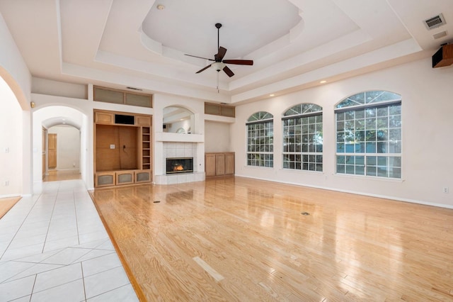 unfurnished living room featuring a raised ceiling, built in shelves, ceiling fan, and light tile patterned floors