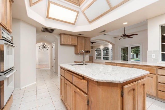 kitchen with french doors, white double oven, sink, light tile patterned floors, and a center island with sink