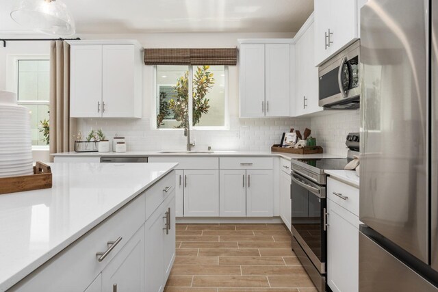 kitchen with white cabinets, a sink, light countertops, stainless steel appliances, and backsplash