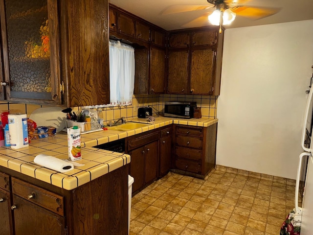 kitchen with a sink, dark brown cabinets, backsplash, and tile counters