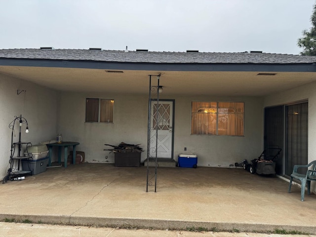 rear view of house featuring a patio, roof with shingles, and stucco siding