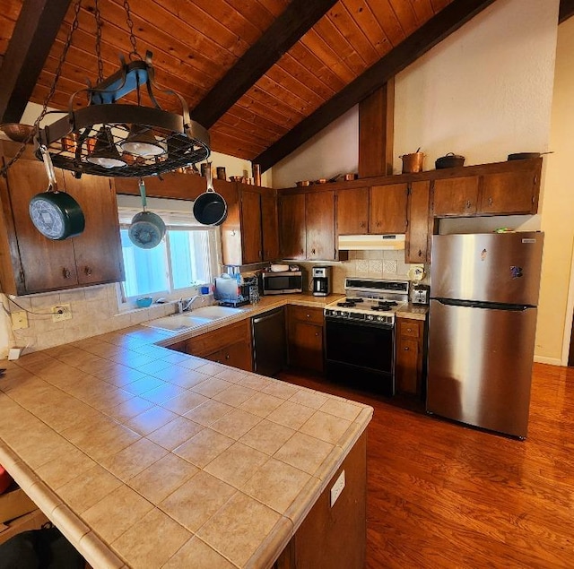 kitchen with appliances with stainless steel finishes, sink, wood-type flooring, tile countertops, and vaulted ceiling with beams