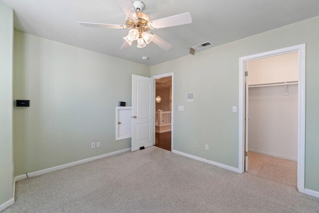 unfurnished bedroom with a walk in closet, baseboards, carpet flooring, and ceiling fan