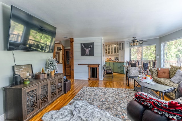 living room with wooden walls, ceiling fan, and light hardwood / wood-style floors