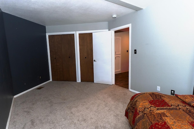 carpeted bedroom featuring a textured ceiling and two closets