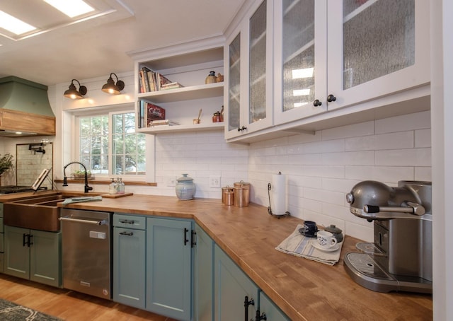 kitchen with wood counters, dishwasher, custom exhaust hood, backsplash, and sink