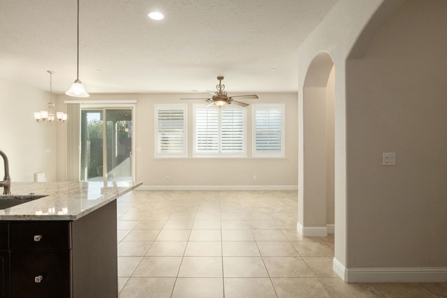 kitchen with light stone countertops, sink, pendant lighting, light tile patterned floors, and ceiling fan with notable chandelier