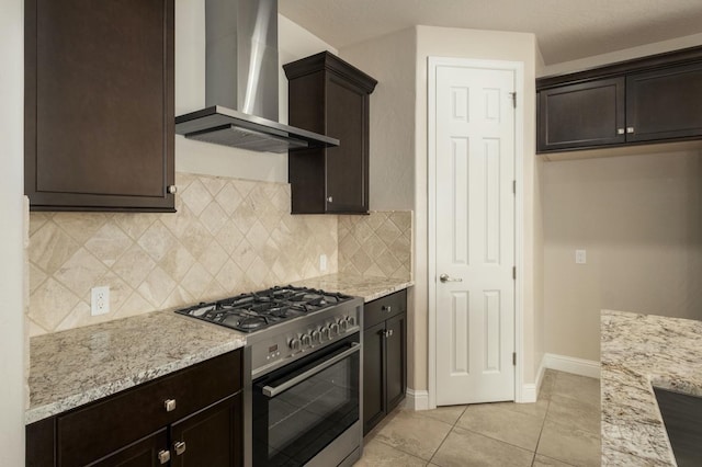 kitchen featuring wall chimney exhaust hood, light stone counters, stainless steel stove, and light tile patterned floors