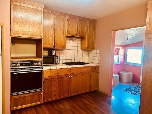 kitchen featuring decorative backsplash, tile countertops, dark wood-style floors, brown cabinets, and black appliances