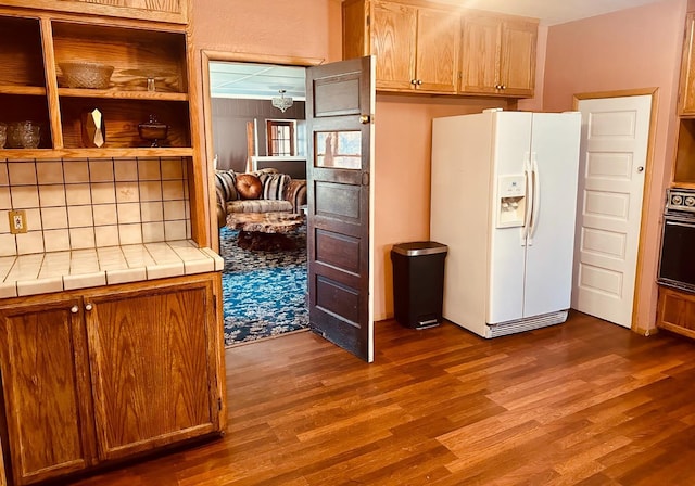 kitchen with white refrigerator with ice dispenser, tile counters, dark wood-type flooring, open shelves, and black oven