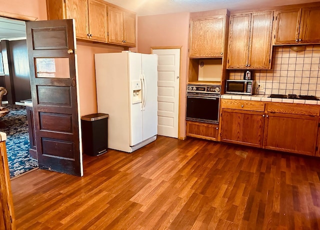 kitchen featuring tile countertops, black appliances, dark wood-style floors, and decorative backsplash