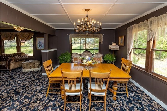 carpeted dining area with plenty of natural light, wood walls, baseboards, and an inviting chandelier