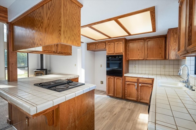 39627 Brandywine Ln, Oakhurst, CA 93644 - kitchen with black appliances, a wood stove, decorative backsplash, light wood-type flooring, and brown cabinetry
