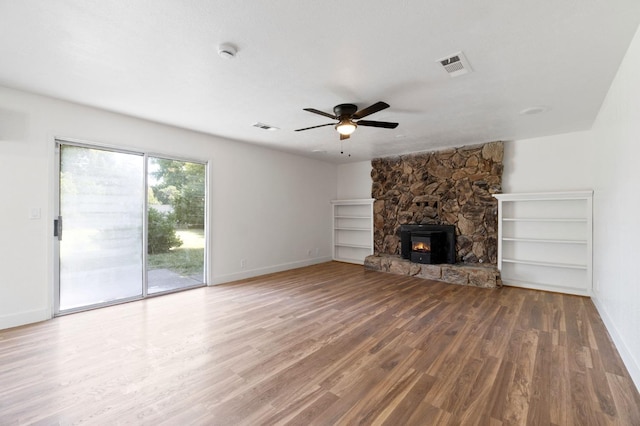 unfurnished living room with a stone fireplace, wood-type flooring, and ceiling fan