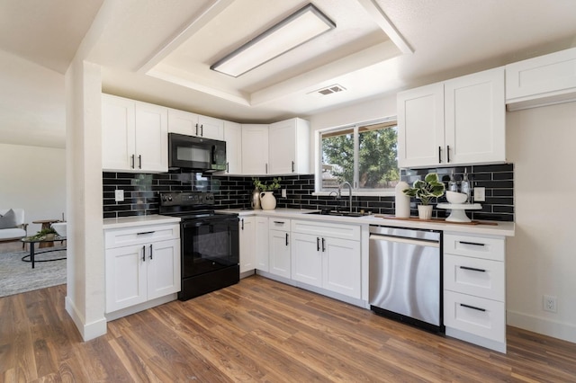 kitchen with sink, white cabinetry, dark hardwood / wood-style floors, black appliances, and a raised ceiling