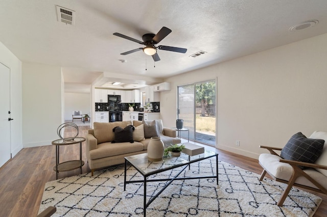 living room with ceiling fan, wood-type flooring, and a textured ceiling