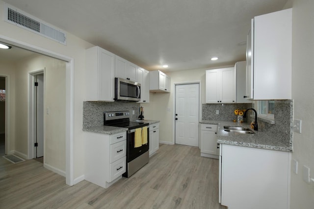 kitchen featuring sink, white cabinetry, light stone counters, appliances with stainless steel finishes, and light hardwood / wood-style floors