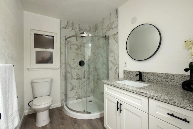 bathroom featuring vanity, wood-type flooring, a shower with shower door, and toilet