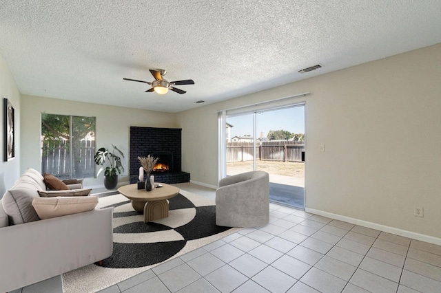 living room with light tile patterned flooring, a fireplace, ceiling fan, and a textured ceiling