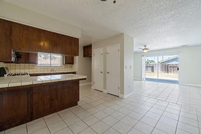 kitchen with light tile patterned flooring, ceiling fan, tasteful backsplash, stove, and tile counters