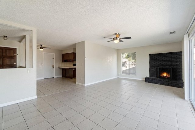 unfurnished living room with a textured ceiling, ceiling fan, a brick fireplace, and light tile patterned floors