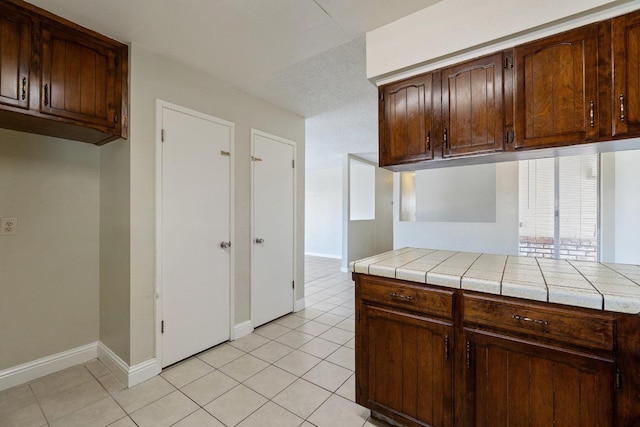 kitchen featuring light tile patterned flooring, tile counters, and dark brown cabinetry