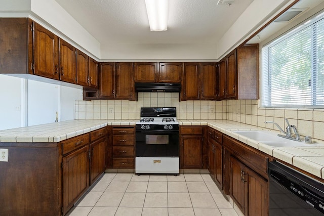 kitchen with sink, tile countertops, black dishwasher, gas range oven, and kitchen peninsula