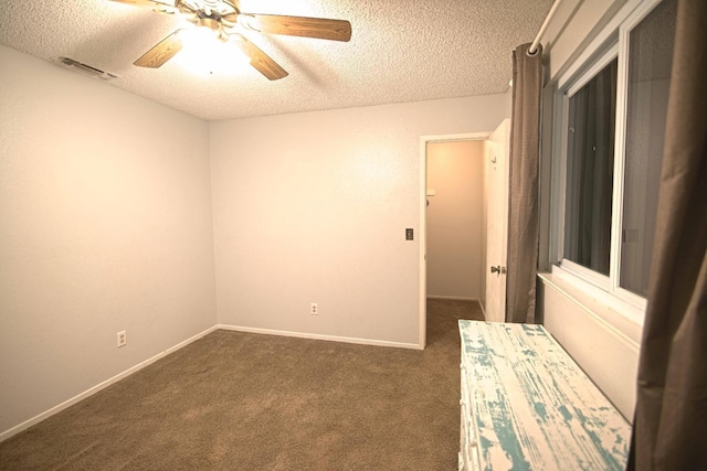 spare room featuring ceiling fan, dark carpet, and a textured ceiling