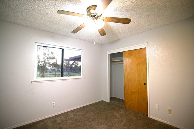 unfurnished bedroom featuring dark colored carpet, a textured ceiling, a closet, and ceiling fan