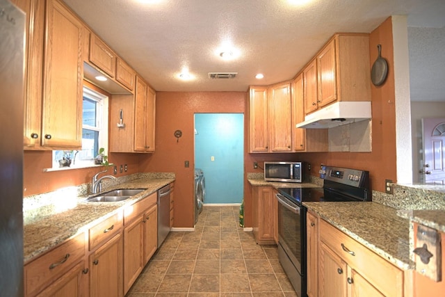 kitchen featuring light stone countertops, a textured ceiling, stainless steel appliances, sink, and washing machine and clothes dryer