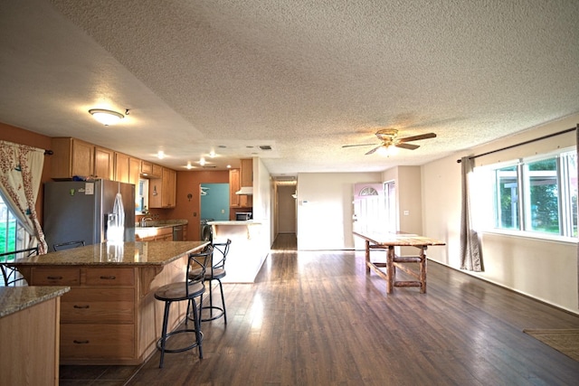 kitchen with a breakfast bar, stainless steel refrigerator with ice dispenser, a textured ceiling, and dark wood-type flooring