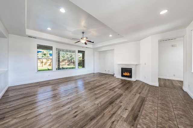 unfurnished living room with a tray ceiling, ceiling fan, and dark wood-type flooring