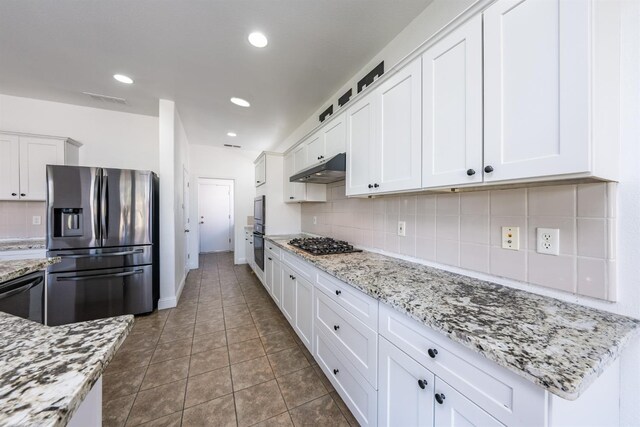 kitchen with white cabinets, dark tile patterned flooring, light stone countertops, tasteful backsplash, and stainless steel appliances