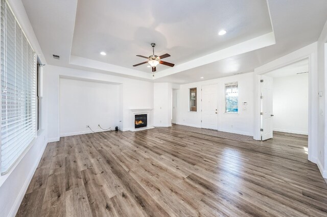 unfurnished living room featuring hardwood / wood-style floors, a raised ceiling, and ceiling fan